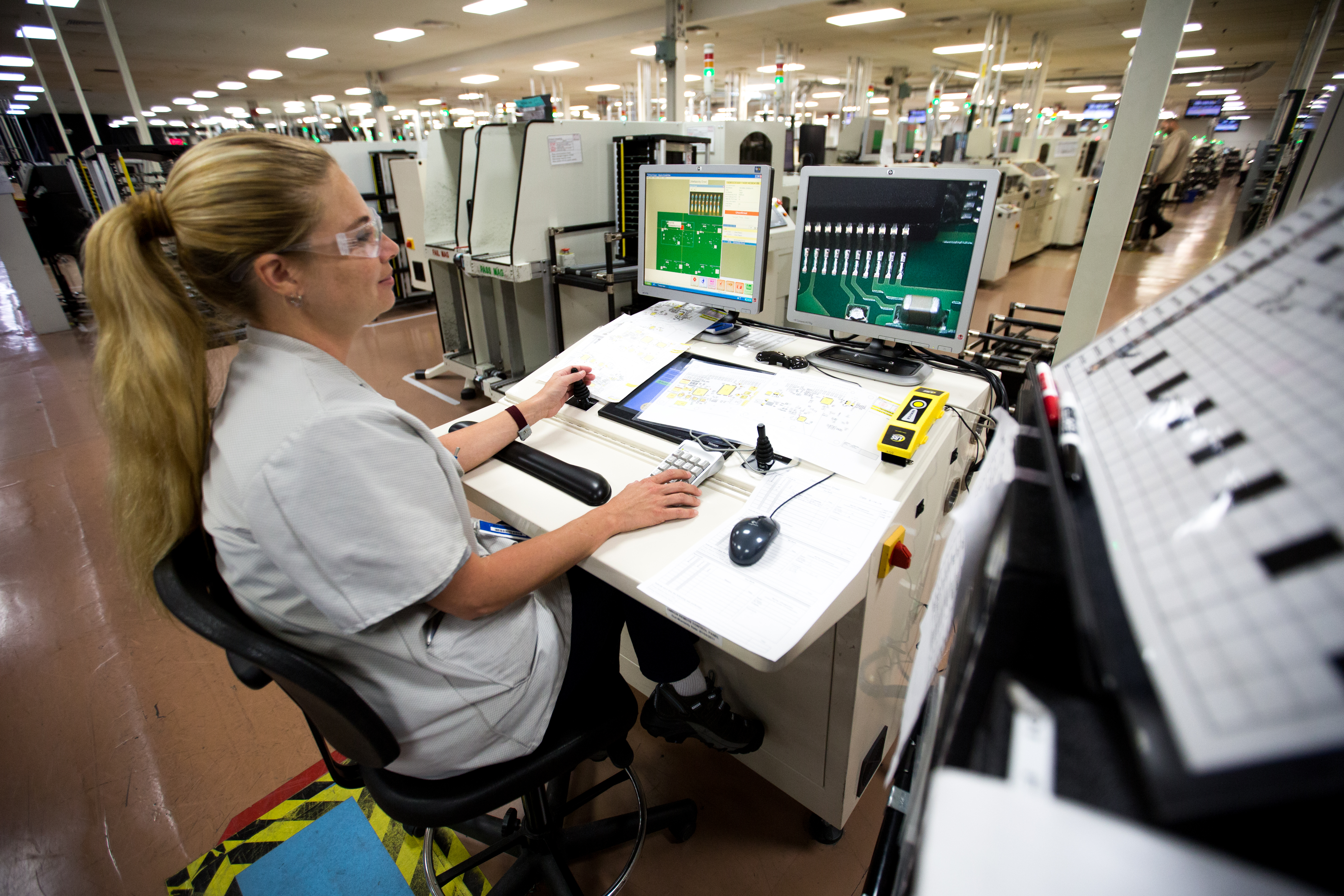A DENSO technician monitors automated optical inspection screens showing circuit board images on the production floor.